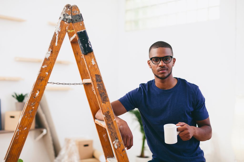 Young man leaning on step ladder having a coffee break