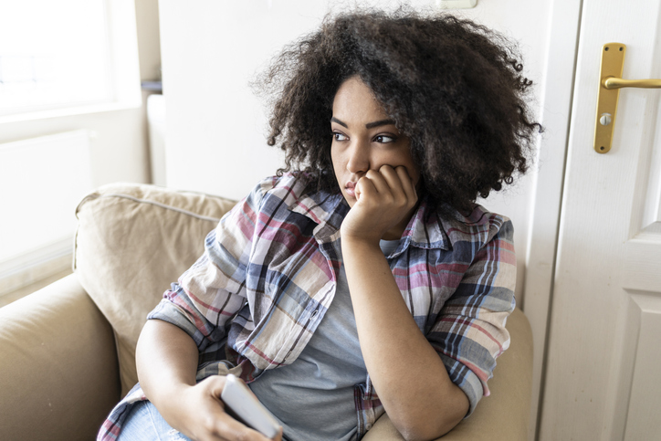 Pensive young woman using smart phone at home