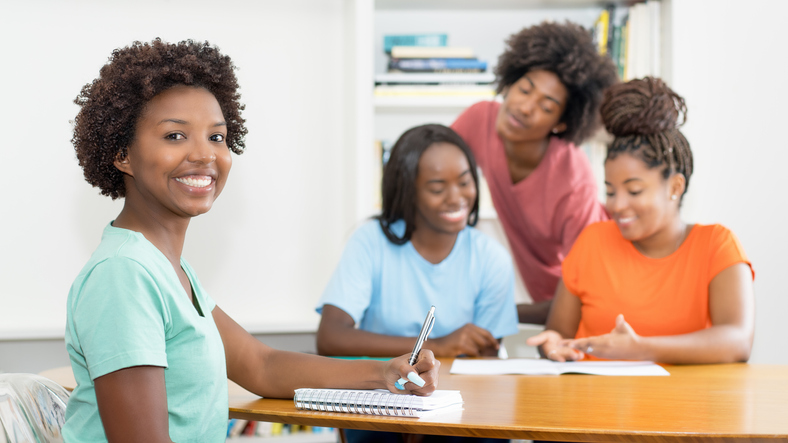 Laughing black female student at desk with group of learning african american students