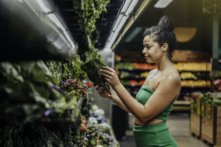 Gen z Hispanic woman grocery shopping and picking greens from the produce section of a grocery store,