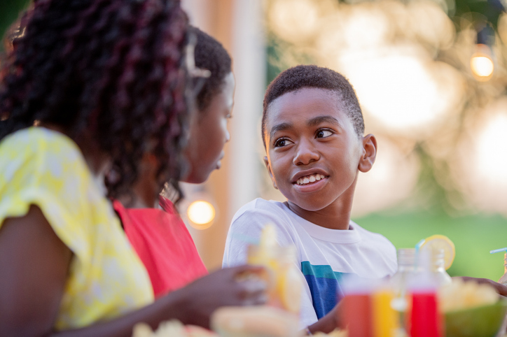 Happy Black Family Laughing Together at Backyard BBQ Dinner With Juice and Fruits