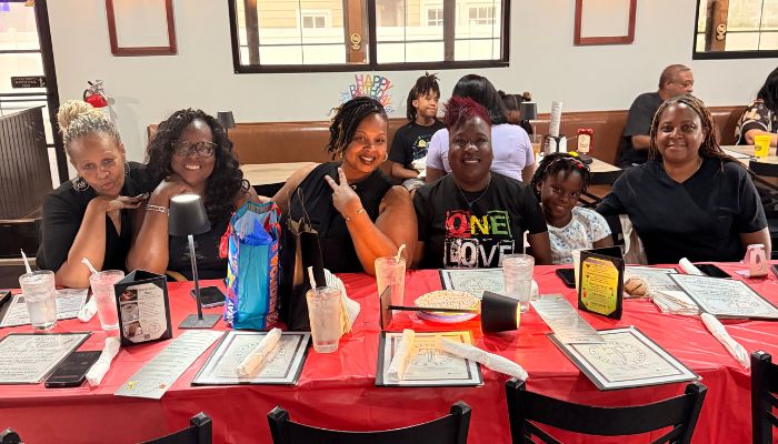 A group of smiling people seated at a table in a restaurant, some wearing shirts with the text "One Love".