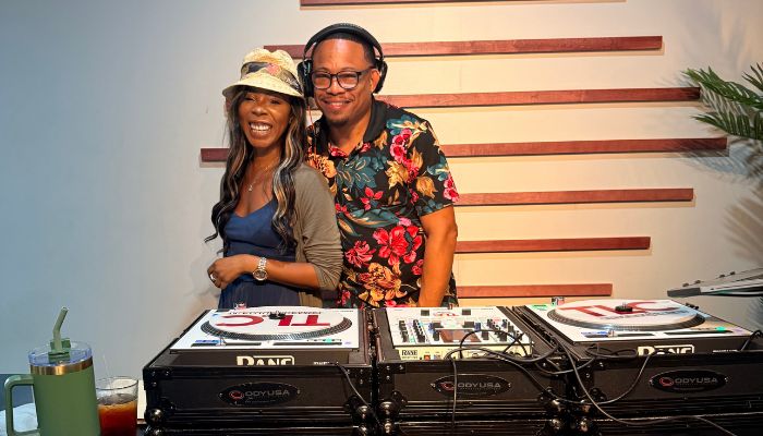 Two people, a man and a woman, smiling and posing together in front of DJ equipment.