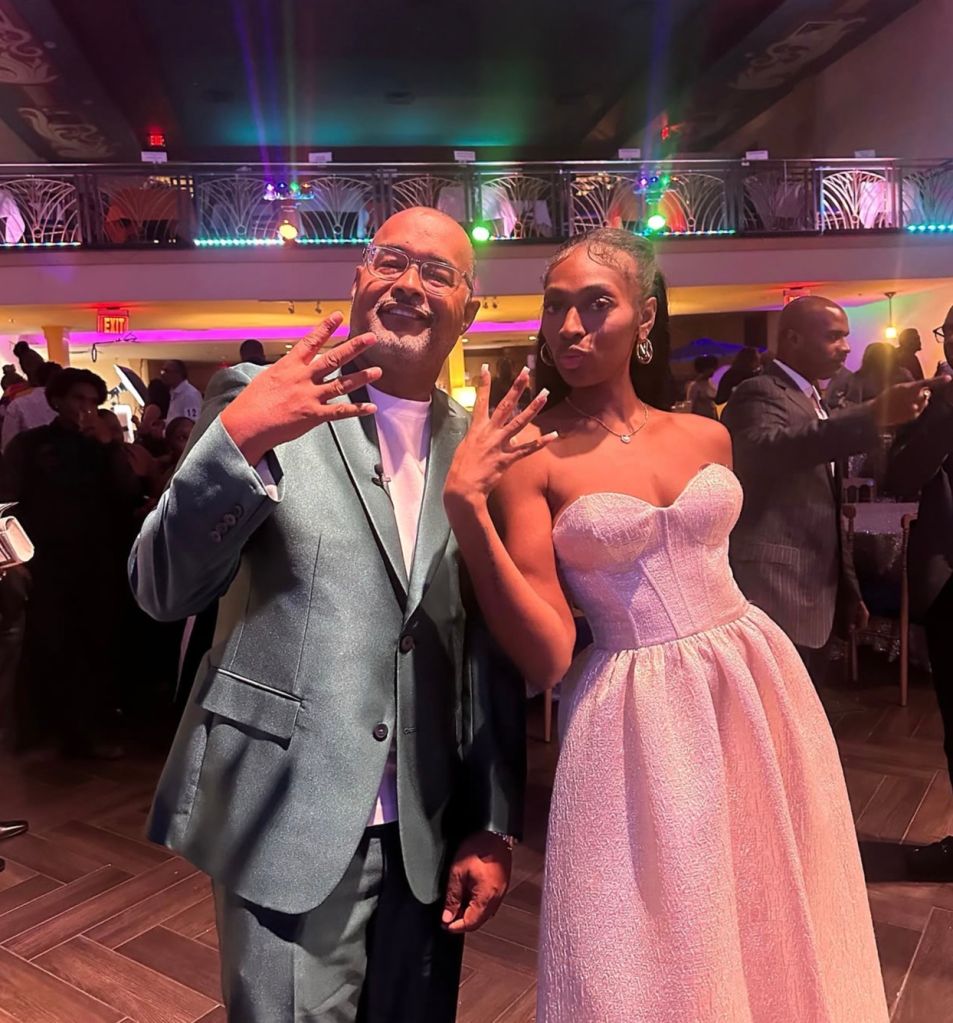 Two people posing at a formal event, with colorful lighting and decorations in the background.