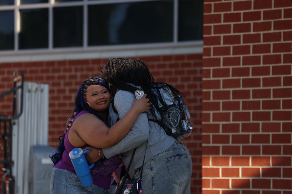 Two people embracing in front of a brick wall.